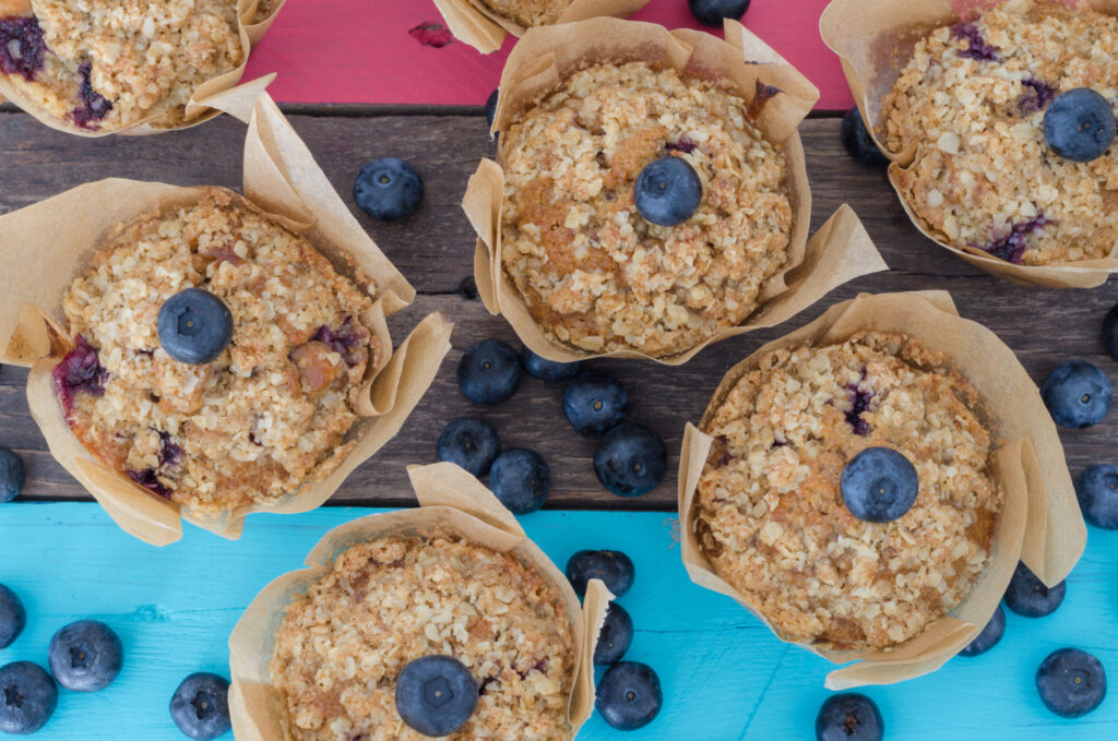 Freshly baked protein muffins topped with blueberries and oats on a white plate.