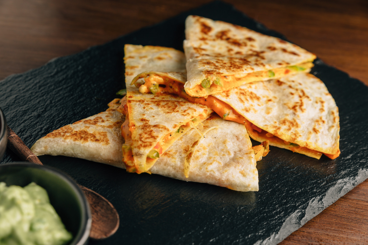 A golden-brown chipotle quesadilla sliced into wedges, filled with melted cheese, grilled chicken, and veggies, served with salsa and guacamole on the side.