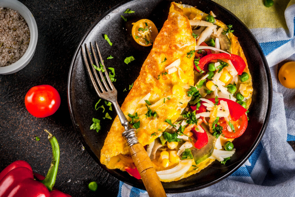 A perfectly cooked omelette folded with fresh vegetables and cheese, served on a plate with a side of toast and a garnish of parsley.