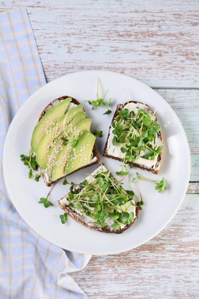 Avocado toast topped with cottage cheese, sliced cherry tomatoes, radishes, and chili flakes on a wooden plate.