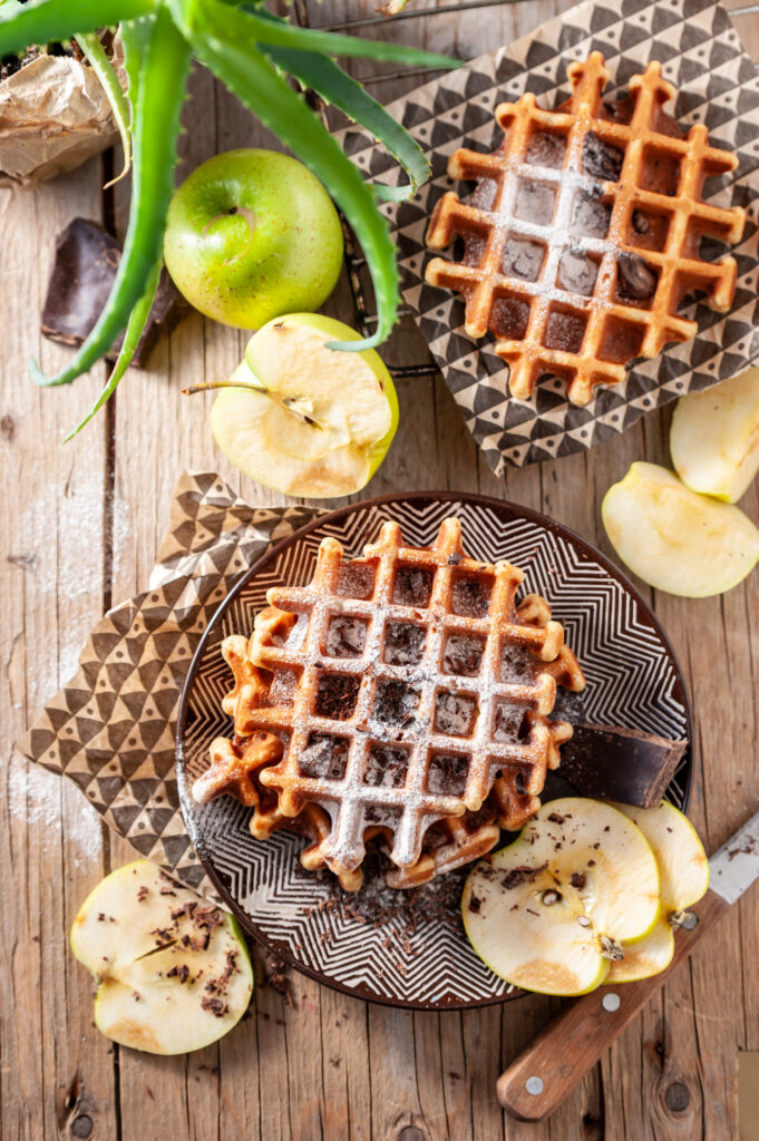 Belgian sugar waffles with caramelized edges, topped with strawberries, powdered sugar, and chocolate sauce.