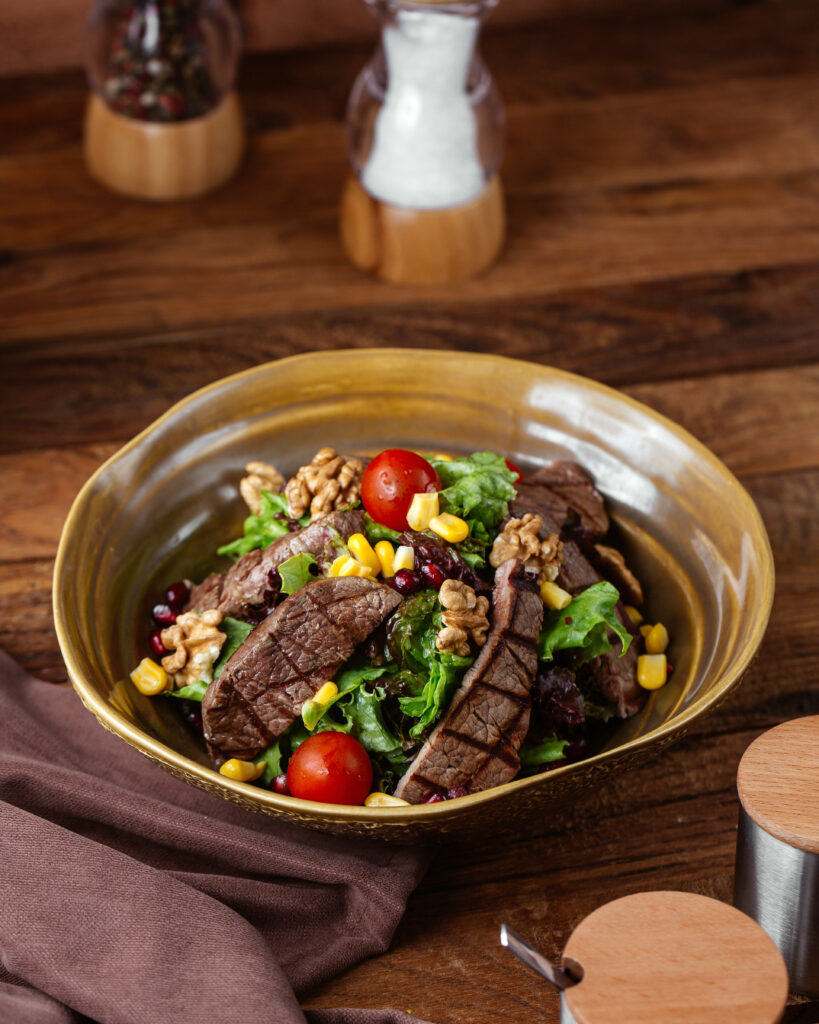 Steak salad with mixed greens, cherry tomatoes, sliced avocado, and balsamic dressing on a white plate.