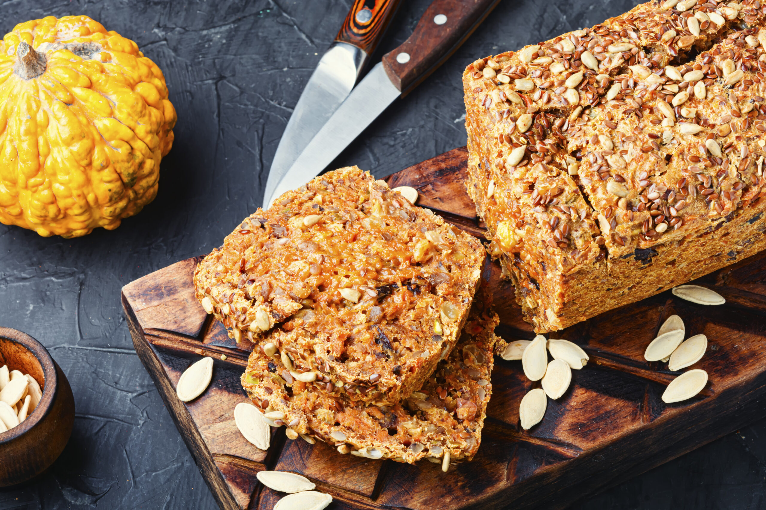 A loaf of muesli bread with visible oats, nuts, and dried fruits, sliced and served on a wooden cutting board.