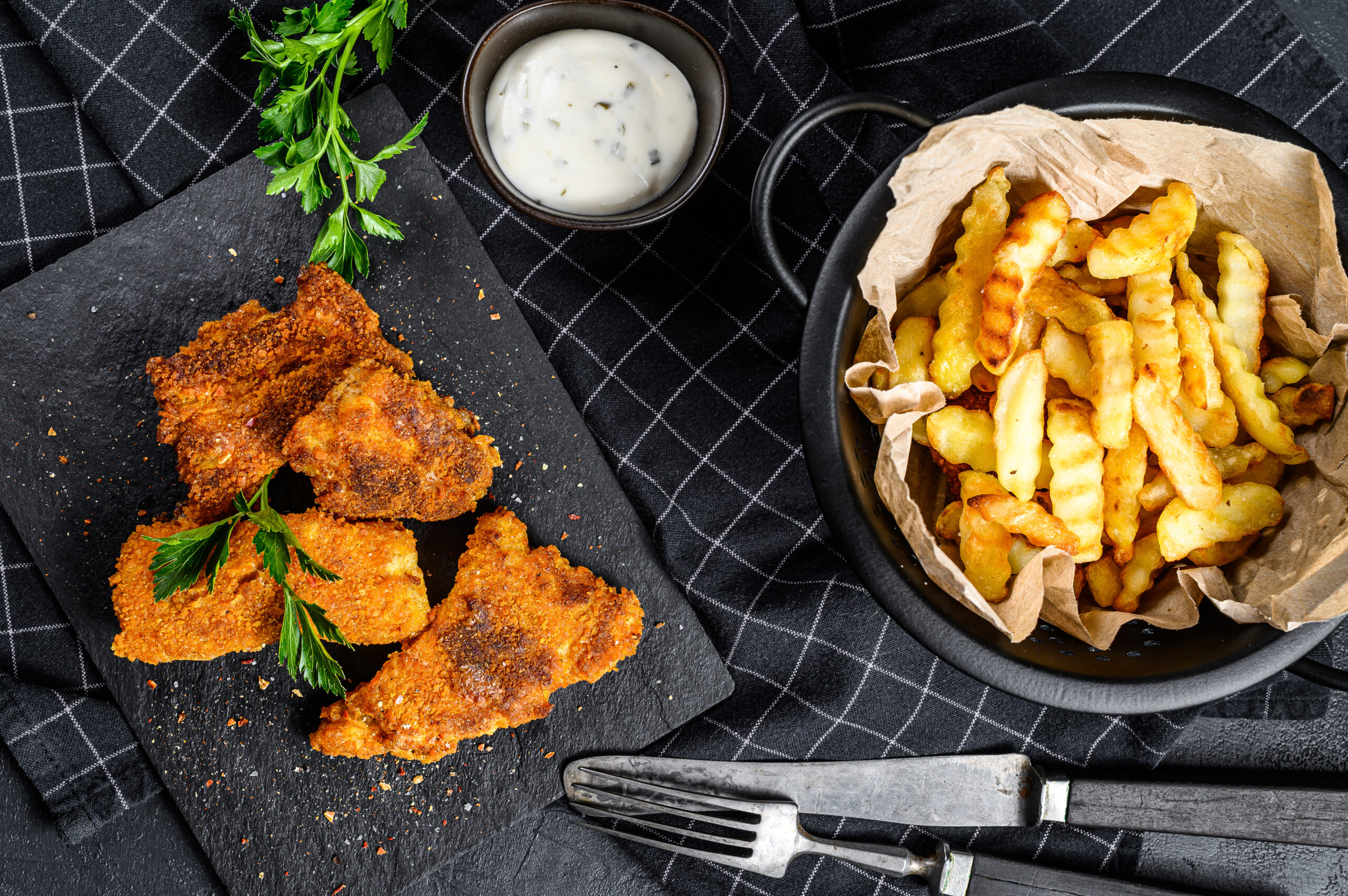 Crispy chicken tenders and golden fries served with dipping sauces on a wooden platter.