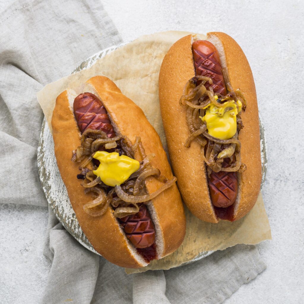 Golden homemade hot dog buns arranged on a cooling rack, brushed with butter and garnished with sesame seeds.