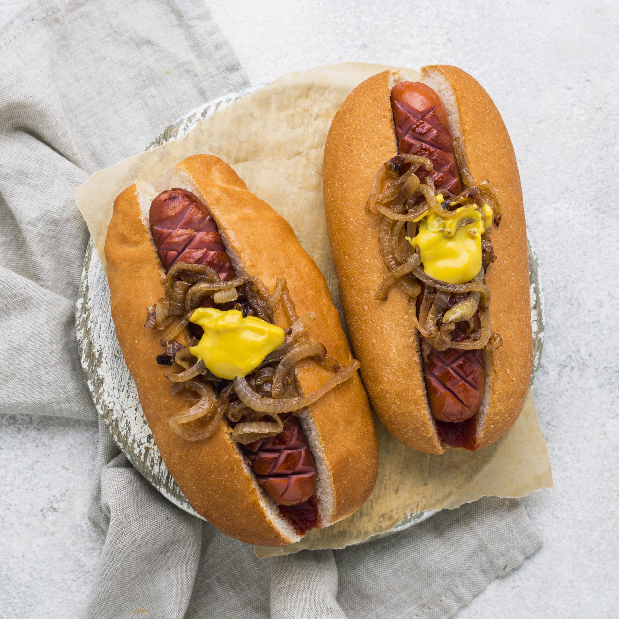 Golden homemade hot dog buns arranged on a cooling rack, brushed with butter and garnished with sesame seeds.