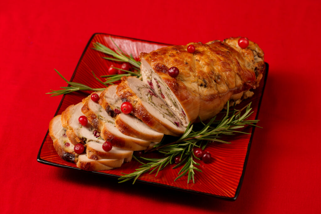 A close-up of bacon-wrapped stuffed chicken breast sliced open, showing the creamy filling and crispy bacon exterior, served with mashed potatoes and greens.