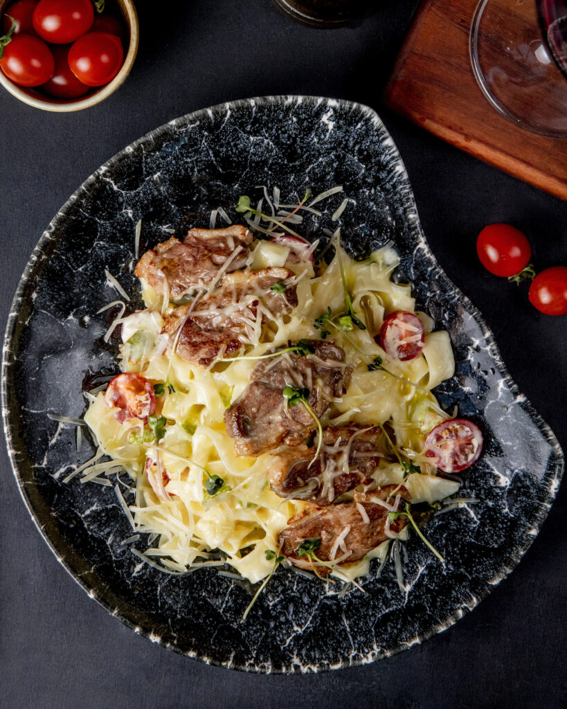 A plate of blackened chicken Alfredo with fettuccine pasta, creamy sauce, and garnished with parsley.