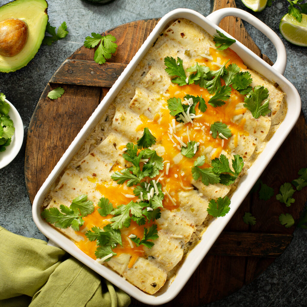 A plate of cheesy chicken enchiladas topped with melted cheese, cilantro, and served with rice and beans on the side.