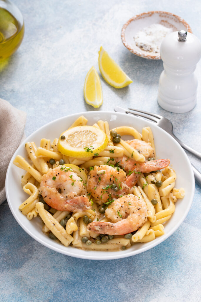 A bowl of shrimp pasta primavera with colorful vegetables like zucchini, cherry tomatoes, and bell peppers, topped with Parmesan and fresh parsley.