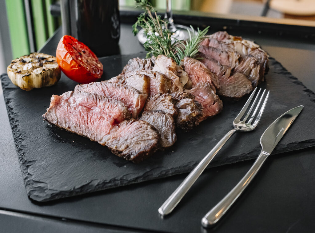 A thick, juicy Delmonico steak cooked to perfection, garnished with a pat of herb butter and served with roasted vegetables and creamy mashed potatoes.