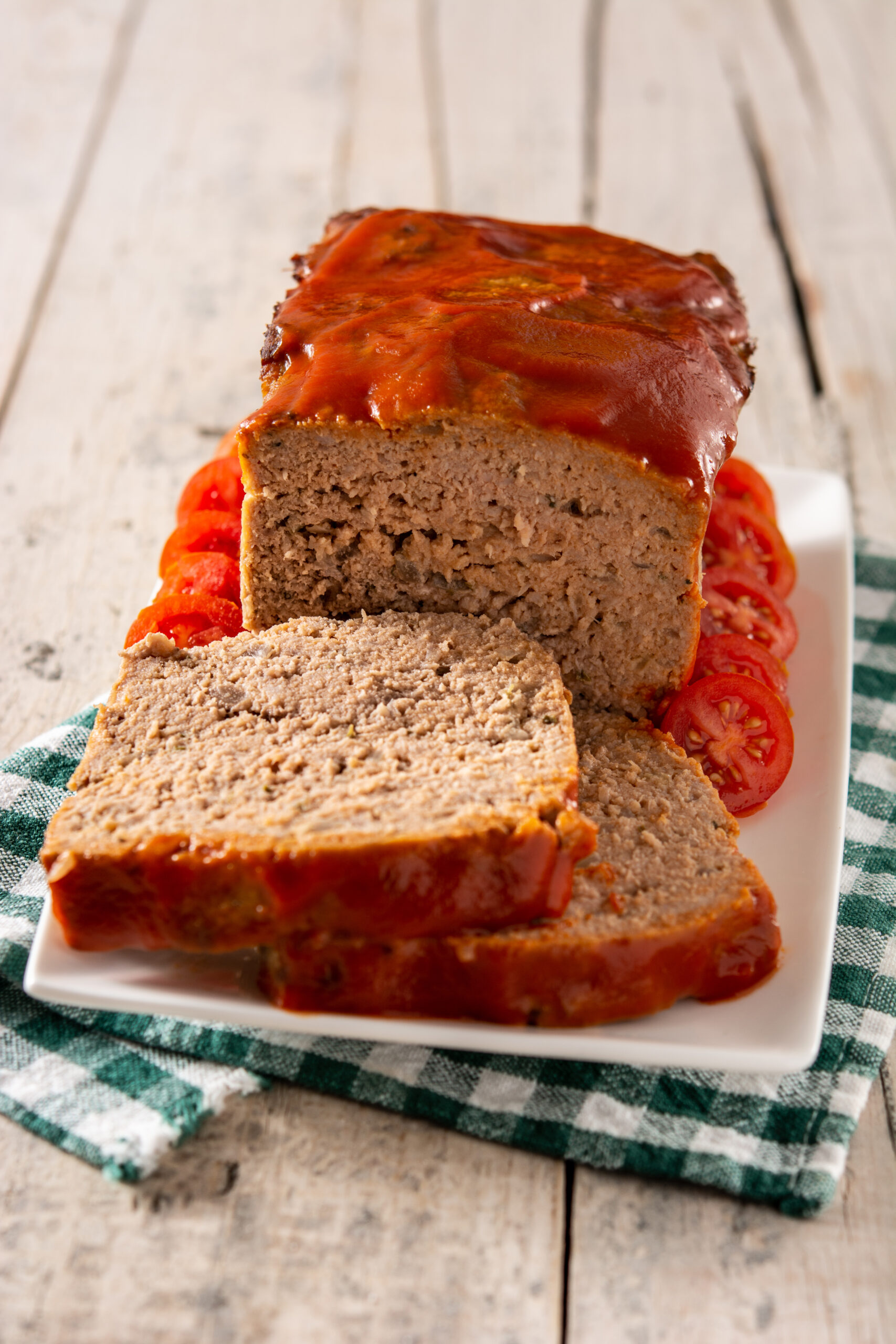 A freshly baked Lipton onion soup meatloaf topped with glaze, sliced to reveal its juicy, tender interior, served on a plate with mashed potatoes and green beans.